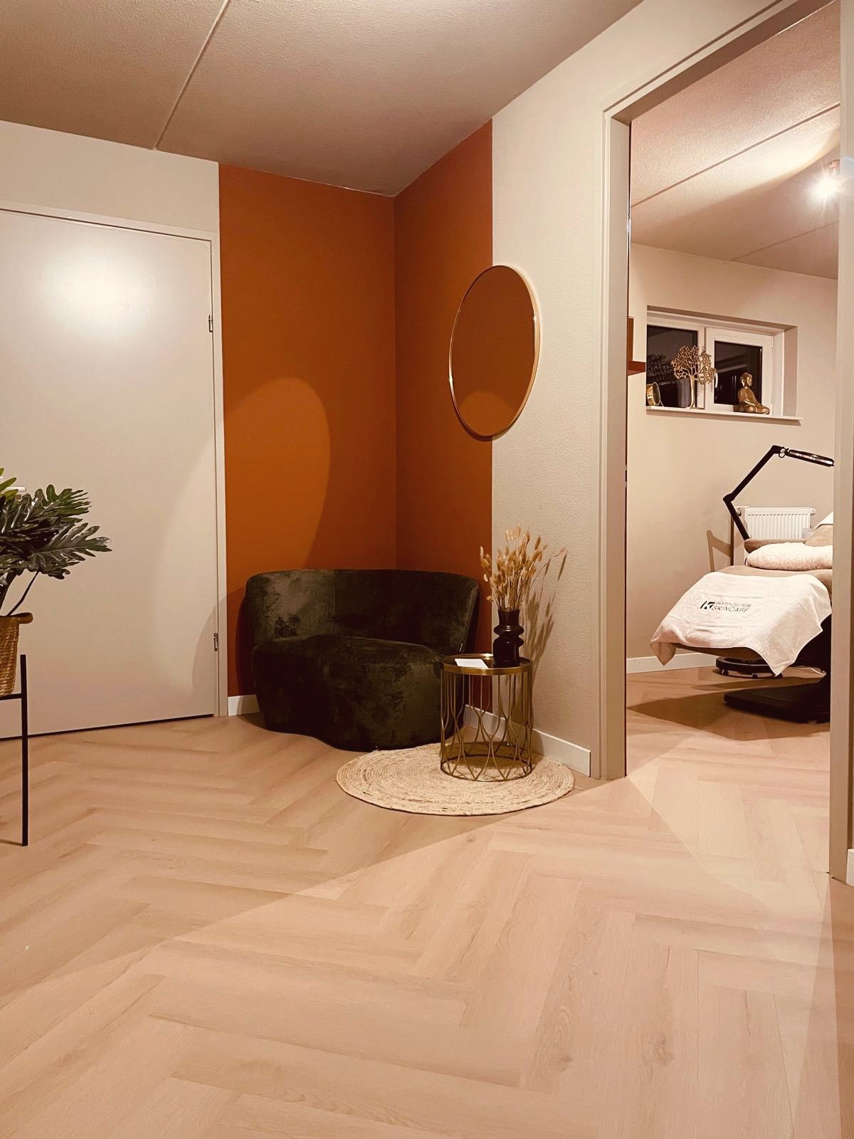Wachtruimte met groene fauteuil voor de terracotta muur en doorkijk naar de behandelkamer